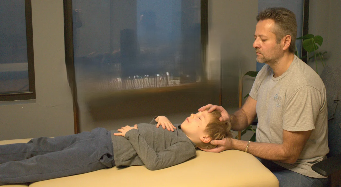 Dr. Alex Kaminsky gently cradling a young boy's head during a craniosacral therapy session for ear-infection support in his Manhattan office.